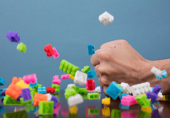 Hand hits to pile of colored toy bricks falling on blue background. Studio shooting. High speed freezing photo