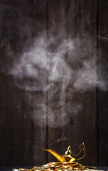 Magic lamp of wishes on stacks of gold coins with smoke coming out from the lamp. Studio shooting.