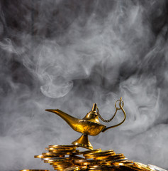 Magic lamp of wishes on stacks of gold coins with smoke coming out from the lamp. Studio shooting.