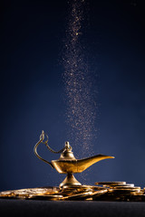 Magic lamp of wishes on stacks of gold coins with golden dust. Studio shooting.