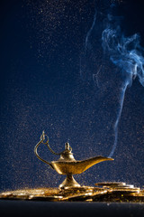Magic lamp of wishes on stacks of gold coins with smoke coming out from the lamp. Studio shooting.