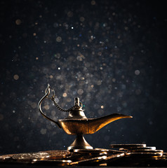 Magic lamp of wishes on stacks of gold coins with golden dust. Studio shooting.