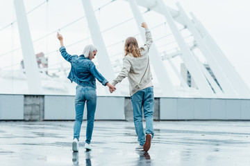 rear view of young couple holding hands and raising fists on street on cloudy day