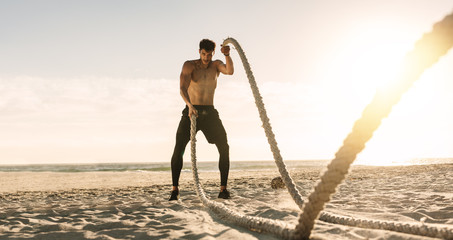 Man doing workout using battling ropes at the beach