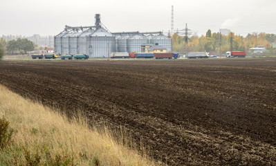 Plowed field in front of the elevator for grain storage. Grain warehouse.