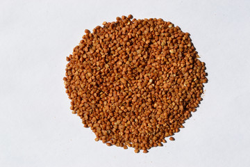 Brown buckwheat laid out on a white table is used as a background or decoration element.