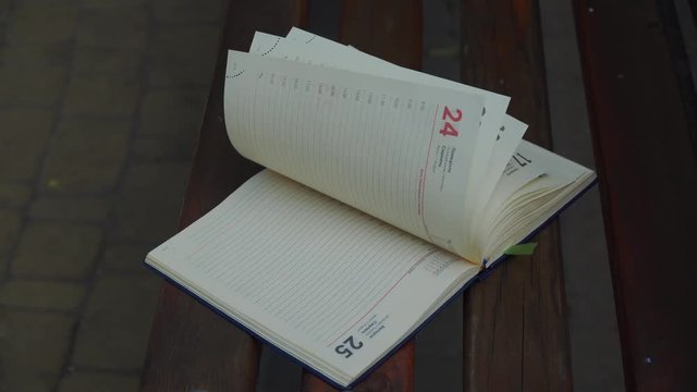 Wind turns the pages of open Notebook lies bench in park, business concept
