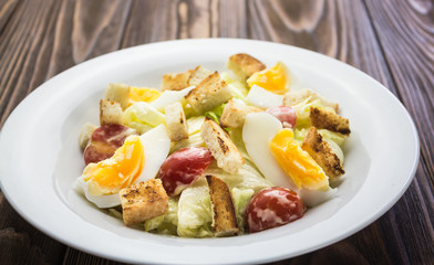 Caesar salad with chicken, in a plate on a wooden background