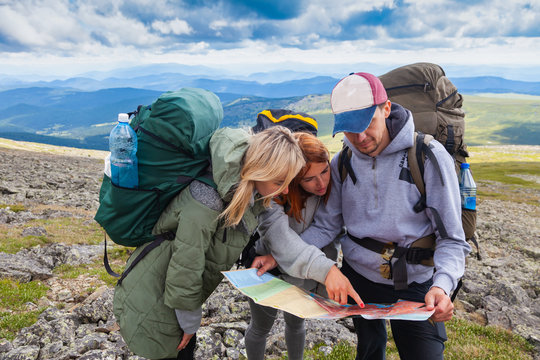 A team of travelers from two women and men with backpacks orient themselves to the terrain, study maps and navigate the route through the mountains. 