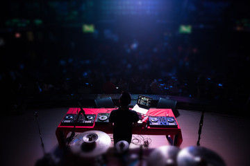 DJ with headphones at night club party under the blue light and people crowd in background