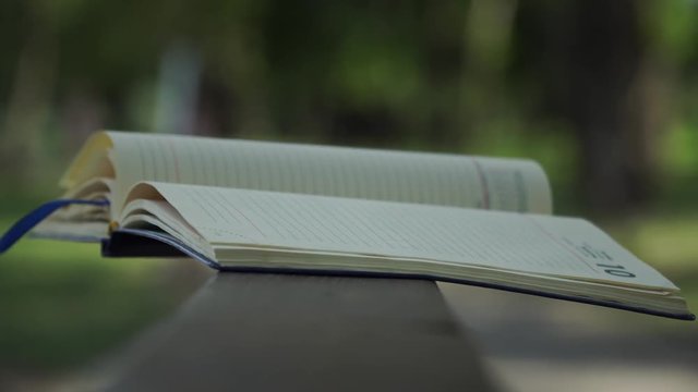 Wind turns the pages of open Notebook lies on wooden handrail in park, business concept