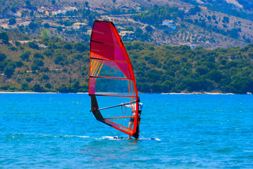 The windsurfer on the board under sail moves at a speed along the surface of the sea