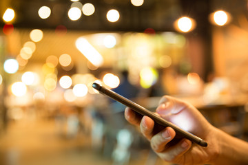 Female hand using Mobile Phone in the pub or  restaurant, night light bokeh Background
