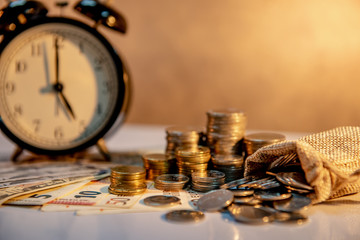 Clock with banknotes and coin stack of international currency on table. Time investment or retirement saving. Business and finance concepts