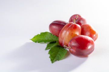 Group of ripe oval Victoria plums from England on white background with leaves