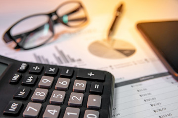 Calculator, eyeglasses, pen, smartphone and summary report paperwork with bar graph, pie chart and table. Financial data analysis. Business planning and management concept