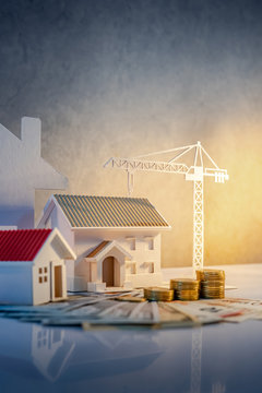 Real estate or property development. Construction business investment concept. Home mortgage loan rate. Coin stack on international banknotes with house and construction crane models on the table.