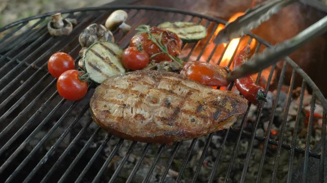 Healthy fish cuisine: fried steaks from white sea fish on the grill with a side dish of grilled vegetables, chili pepper, rosemary, zucchini, cherry tomatoes, cloves of garlic and mushrooms, cooking