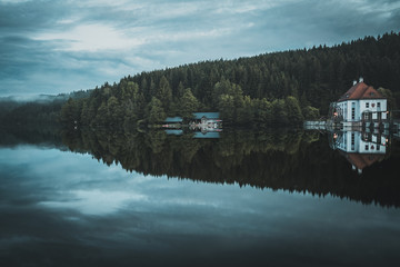 Reflection from houses and trees on the lake with fog and dusk in the background