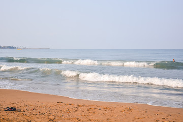 The sea sandy beach in the early morning, on the sea, among the waves, a man is bathing.