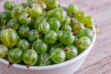 Ripe berries of a gooseberry n white plate on a wooden background close-up. 