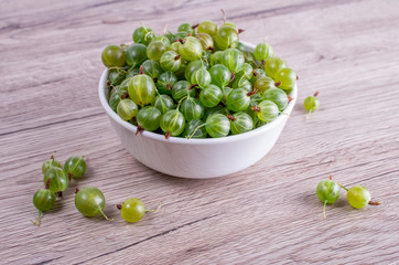 Ripe berries of a gooseberry n white plate on a wooden background with space for insert text. Top view, copy space.