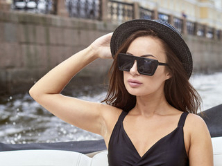 Portrait of a young brunette wearing black glasses and a hat in a boat.