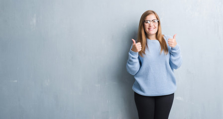 Young adult woman over grey grunge wall wearing glasses success sign doing positive gesture with hand, thumbs up smiling and happy. Looking at the camera with cheerful expression, winner gesture.