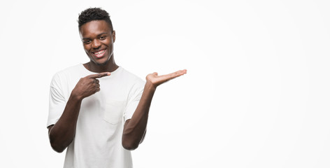 Young african american man wearing white t-shirt amazed and smiling to the camera while presenting...