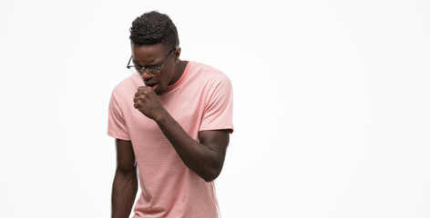 Young african american man wearing pink t-shirt feeling unwell and coughing as symptom for cold or...