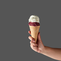 A female hand holds berry sorbet and vanilla ice cream in a waffle cone on a gray background with place for text.