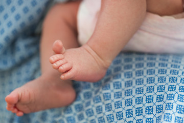 Ножки младенца, крохотной девочки в розовом боди на фоне голубого платья мамы