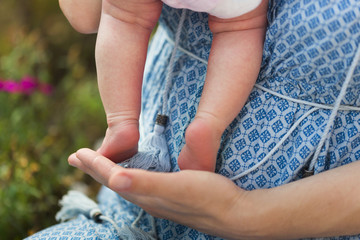 Ножки младенца, крохотной девочки в розовом боди, в руках мамы в голубом платье   - obrazy, fototapety, plakaty