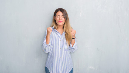 Young adult woman over grey grunge wall wearing fashion business outfit excited for success with arms raised celebrating victory smiling. Winner concept.