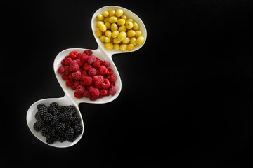 raspberry, blackberries and dogeberry in white plate on black background