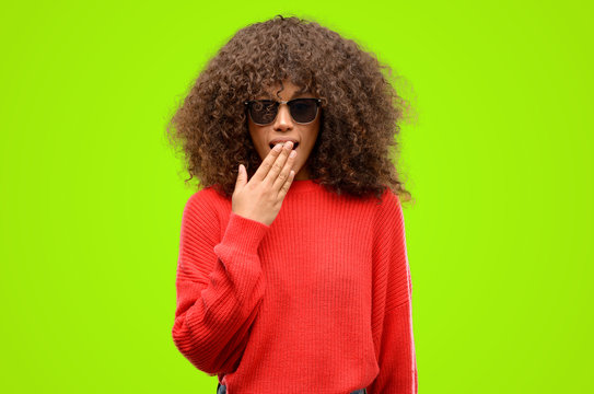 African american woman wearing sunglasses covers mouth in shock, looks shy, expressing silence and mistake concepts, scared