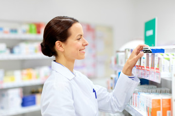 medicine, pharmaceutics, healthcare and people concept - happy female apothecary taking drug from shelf at pharmacy