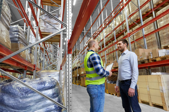 logistic business, shipment and people concept - worker with clipboard and businessman at warehouse