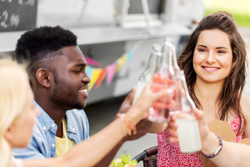 celebration, leisure and people concept - happy friends clinking bottles with non alcoholic drinks at food truck