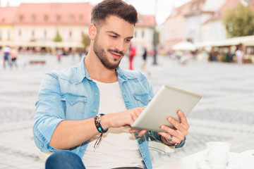 handsome man tapping his tablet while sitting in the city