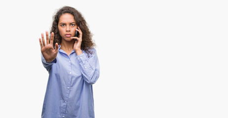 Young hispanic woman using smartphone with open hand doing stop sign with serious and confident expression, defense gesture