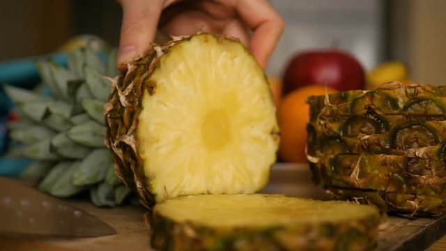 Man slicing  ananas , pineapple with knife on wooden board with fruits and vegetables on background. Close-up.