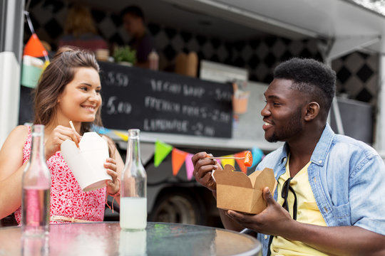 leisure and people concept - happy mixed race couple eating and talking at food truck