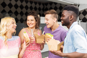 leisure and people concept - happy friends with drinks eating and talking at food truck