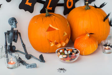 halloween, holidays and decoration concept - jack-o-lantern or carved pumpkins with candies and festive garland on white background