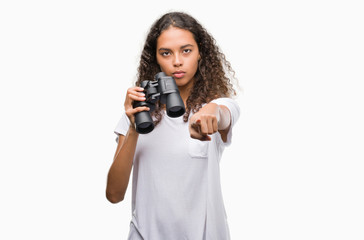 Young hispanic woman looking through binoculars pointing with finger to the camera and to you, hand...