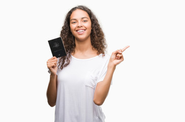Young hispanic woman holding passport of Australia very happy pointing with hand and finger to the...