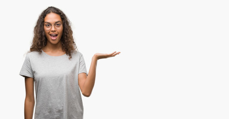 Beautiful young hispanic woman wearing glasses smiling cheerful presenting and pointing with palm...