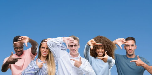 Composition of group of friends over blue blackground smiling making frame with hands and fingers...