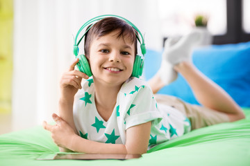 childhood, technology and people concept - smiling boy with tablet pc computer and headphones lying on bed at home - Powered by Adobe